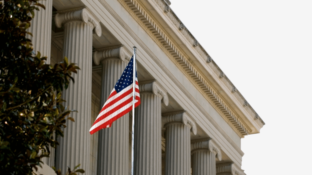 American flag flying in front of a neoclassical government building with tall stone columns, symbolizing public service, governance, and institutional leadership.